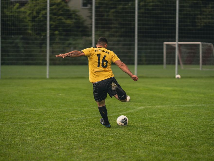 man in yellow and black soccer jersey kicking soccer ball on green grass field during daytime